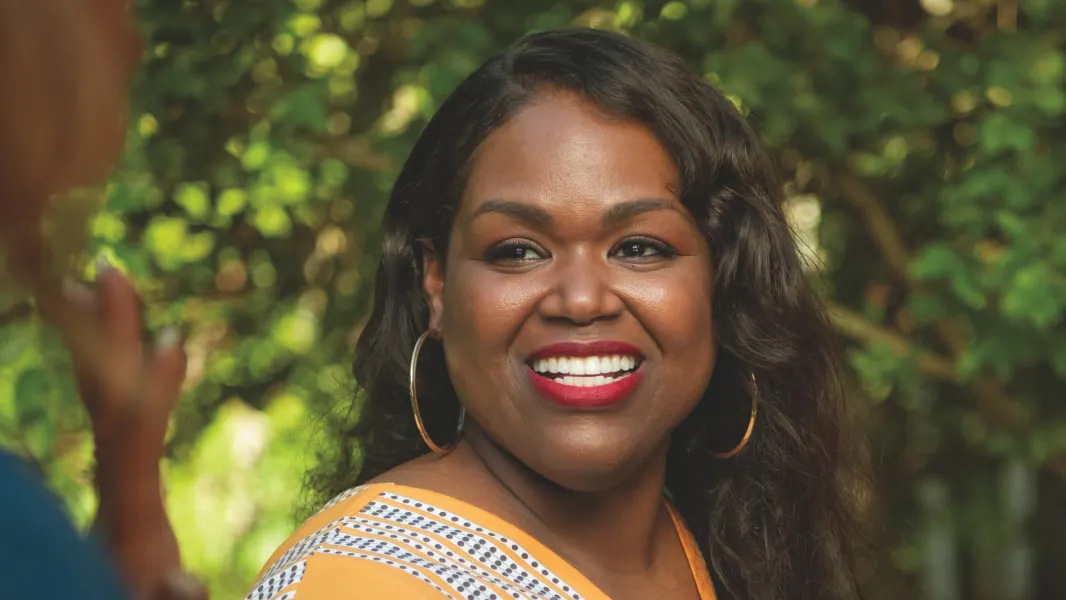 Smiling BENLYSTA patient Nadine wearing a yellow shirt while standing outside