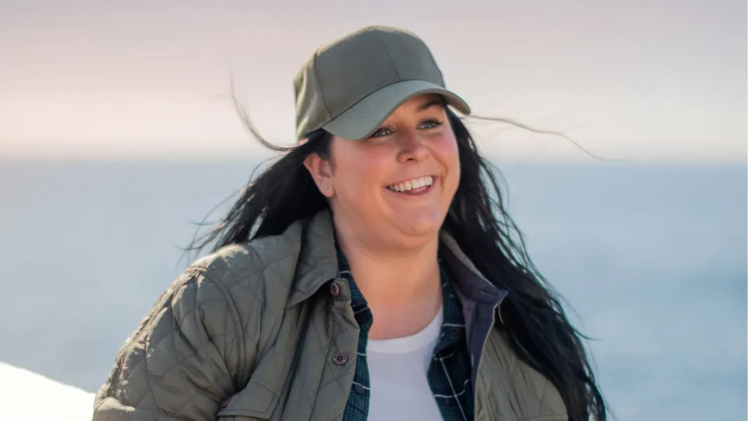 BENLYSTA patient Morgan wearing a gray hat and jacket standing next to the water
