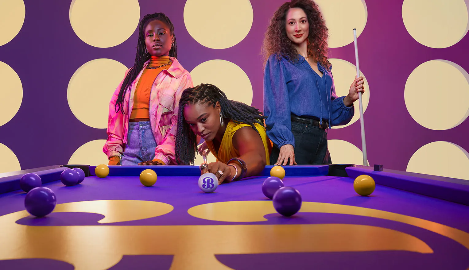 Woman shooting a gold pool ball while two other women stand behind her