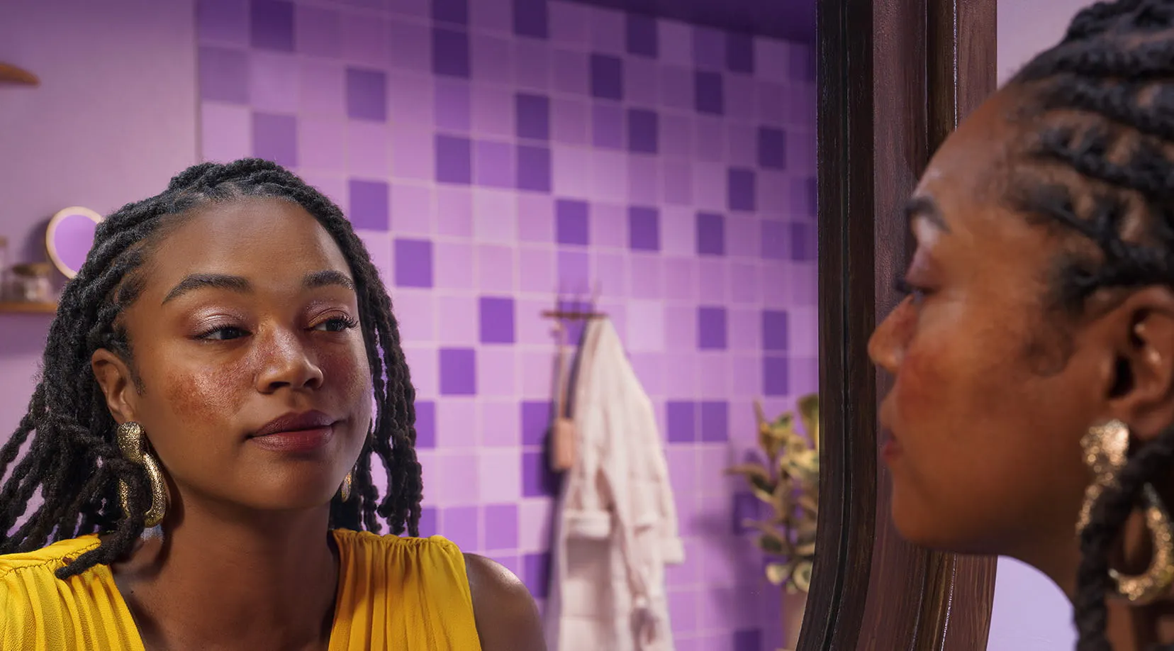 Woman wearing a yellow shirt looking at her reflection in a bathroom mirror