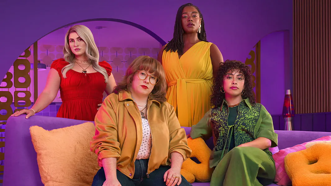 Two women sitting on a pink couch with two women standing behind them