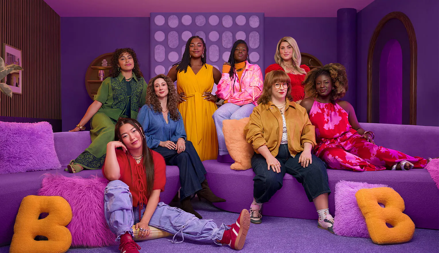 Group of women sitting on and standing behind a purple couch with purple pillows and yellow B-shaped pillows