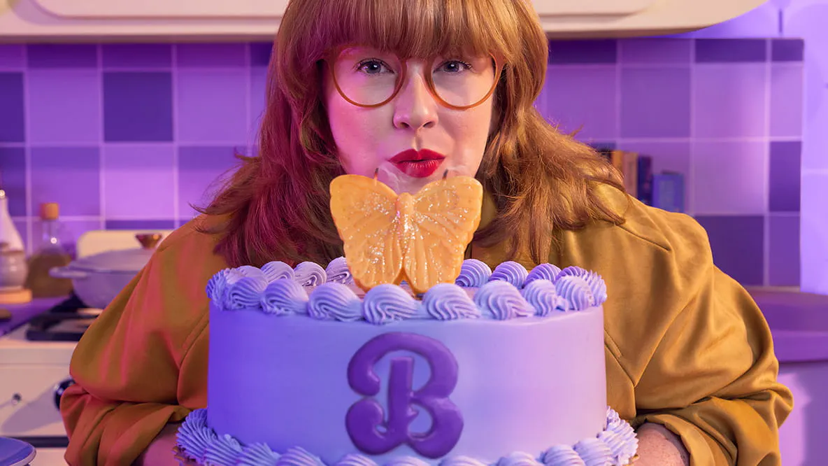 Woman blowing out a butterfly-shaped candle on a purple cake with the letter B on it