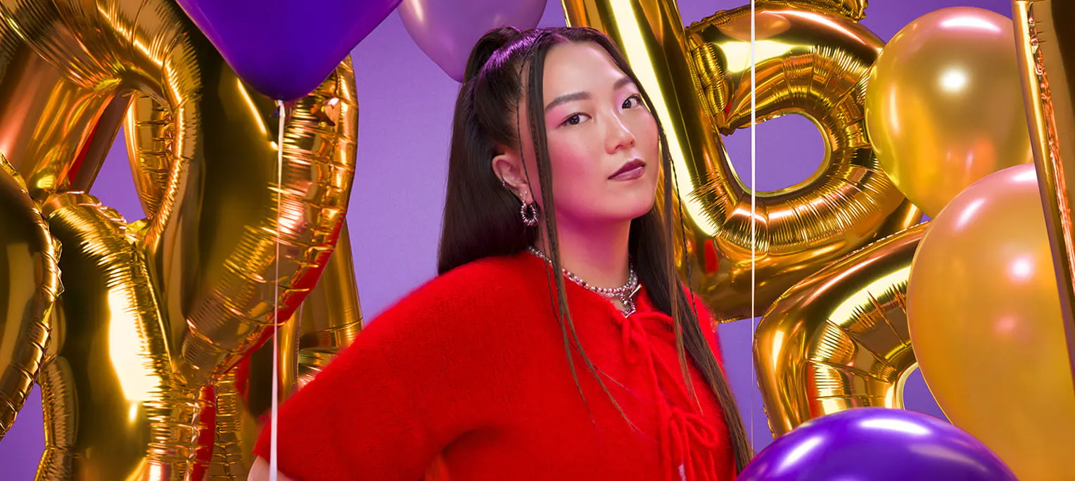 Woman in a red shirt standing in front of gold balloons shaped like the letter B