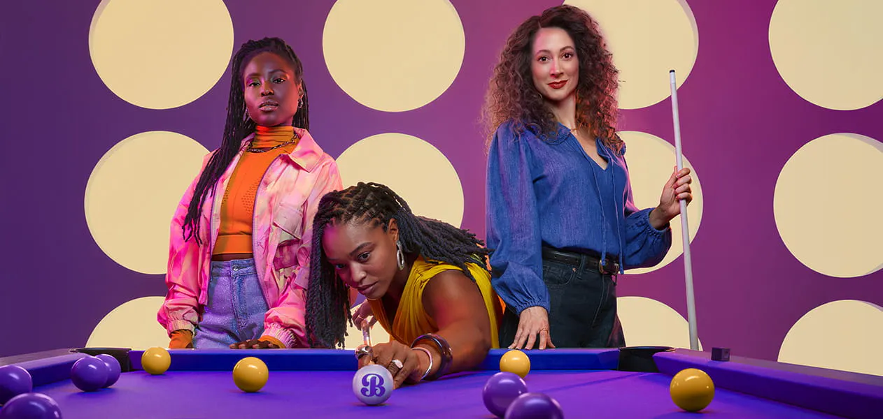 Woman shooting a gold pool ball while two other women stand behind her Woman shooting a gold pool ball while two other women stand behind her