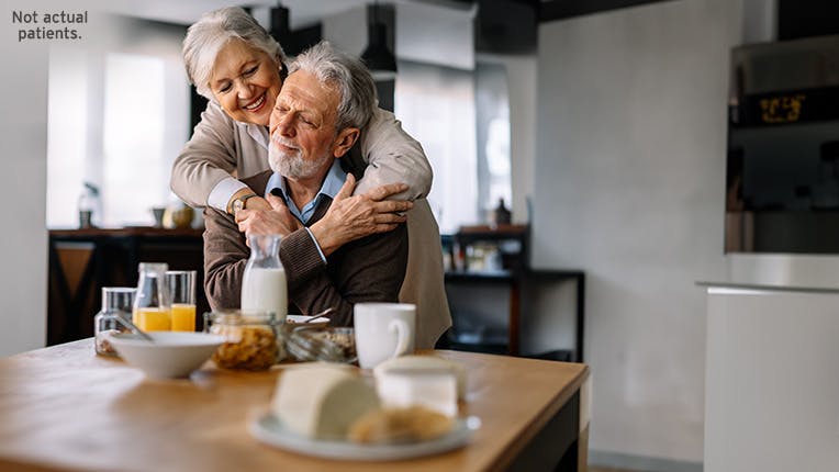 Woman standing with her arms around a man seated at table