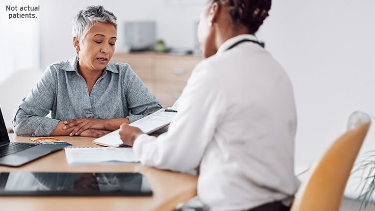 Woman talking to a person acting as a doctor with a laptop sitting at a desk