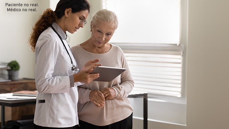 Una mujer en calidad de médica sosteniendo una tableta mientras habla con una mujer