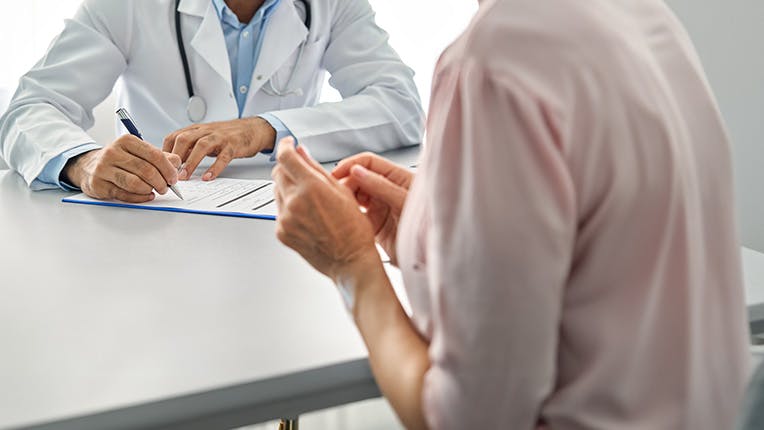 Médico que escribe en un portapapeles mientras habla con una mujer