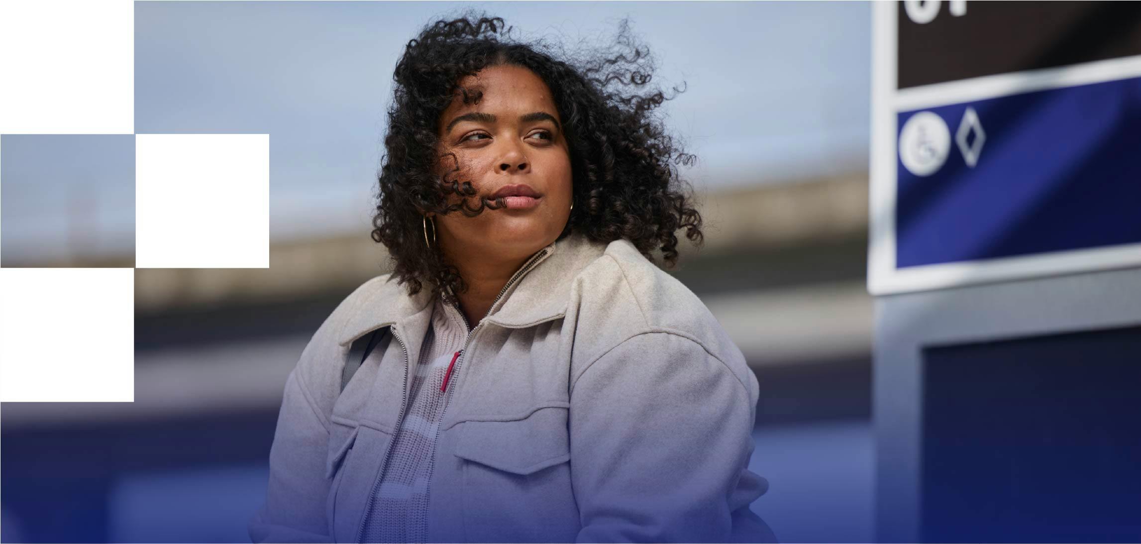 Woman with dark curly hair wearing a tan jacket while waiting at a train station Woman with dark curly hair wearing a tan jacket while waiting at a train station