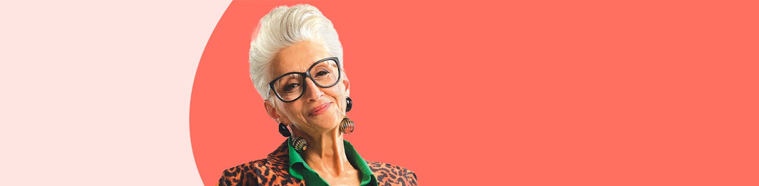 An older woman smiling wearing black framed glasses and an animal print coat.