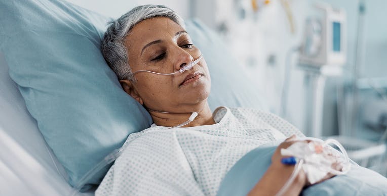 Older female patient lying in a hospital bed with oxygen tubes in her nostrils and an IV in her hand Older female patient lying in a hospital bed with oxygen tubes in her nostrils and an IV in her hand