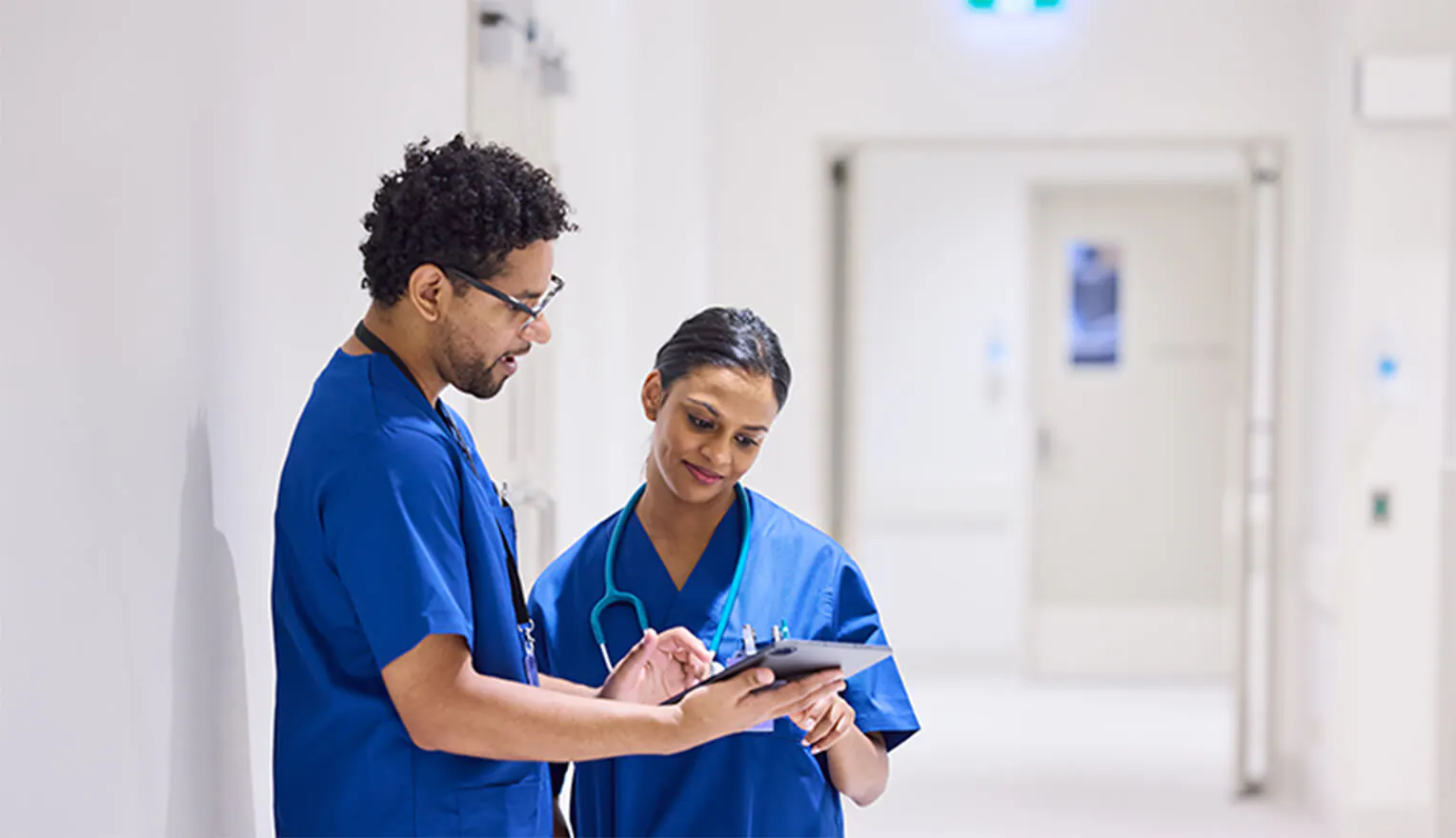 Two healthcare workers in blue scrubs looking at tablet. Two healthcare workers in blue scrubs looking at tablet.