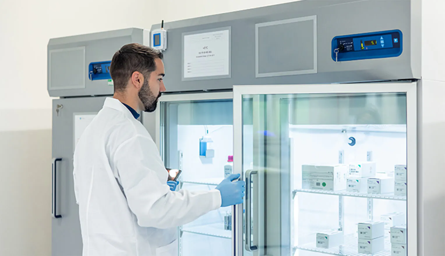 A scientist wearing a white lab coat opening a laboratory refrigerator. A scientist wearing a white lab coat opening a laboratory refrigerator.
