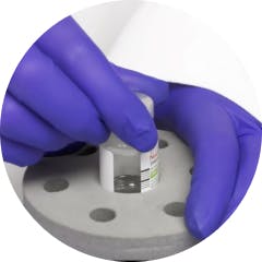 Gloved hand placing NUCALA lyophilized powder vial in reconstitution device Gloved hand placing NUCALA lyophilized powder vial in reconstitution device