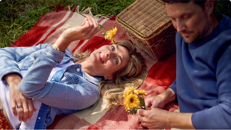 Man and woman lying on picnic blanket holding yellow flowers
