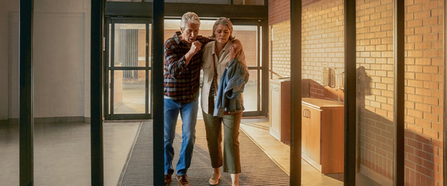 Older couple walking into the emergency room as the man is coughing Older couple walking into the emergency room as the man is coughing