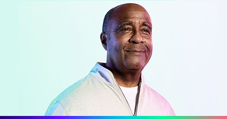 An older black male wearing a gray quarter zip sweater with a white shirt underneath.