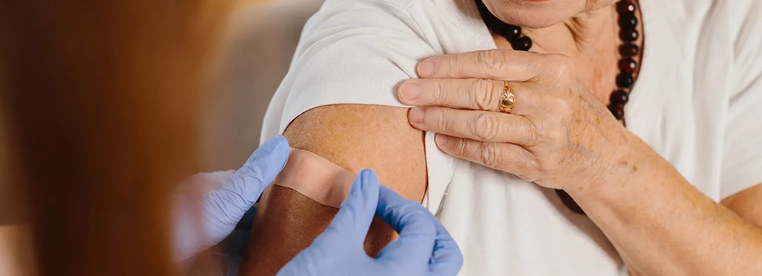 Healthcare provider placing a bandage on a patient's upper arm after they've received a vaccine