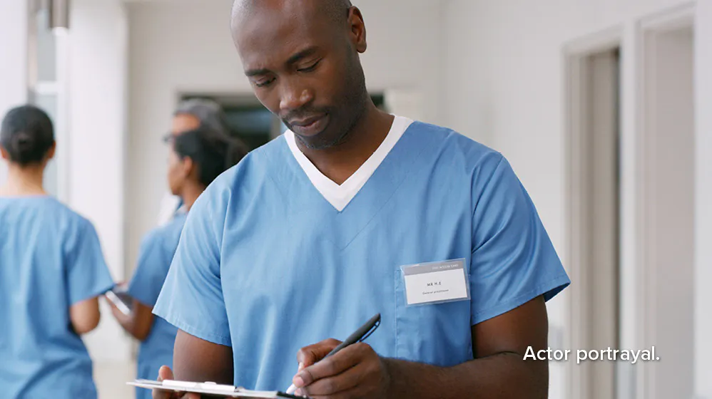 Actor portrayal: male nurse wearing blue scrubs writing on a clipboard