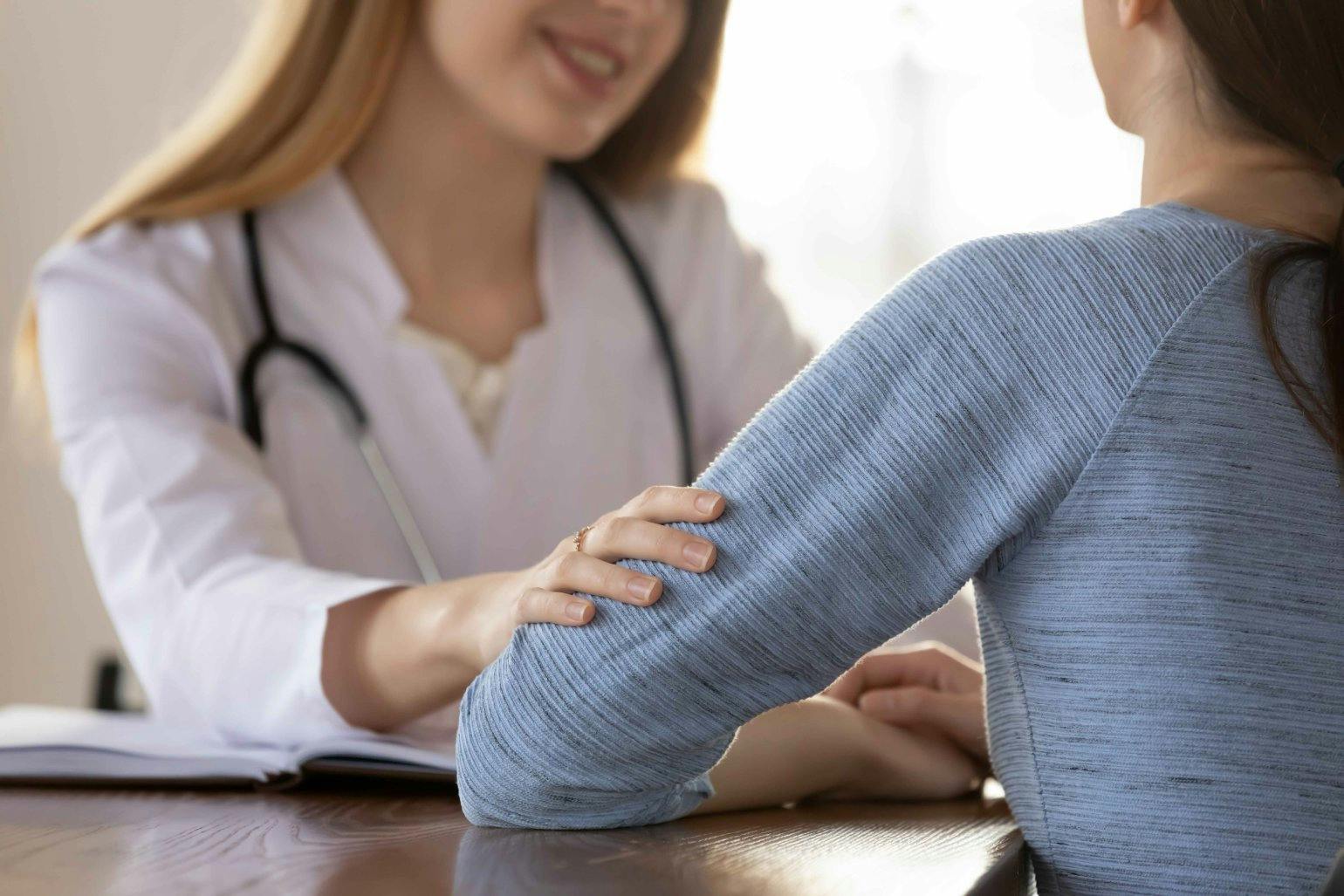 Caring female doctor wearing uniform comforting young woman patient at meeting