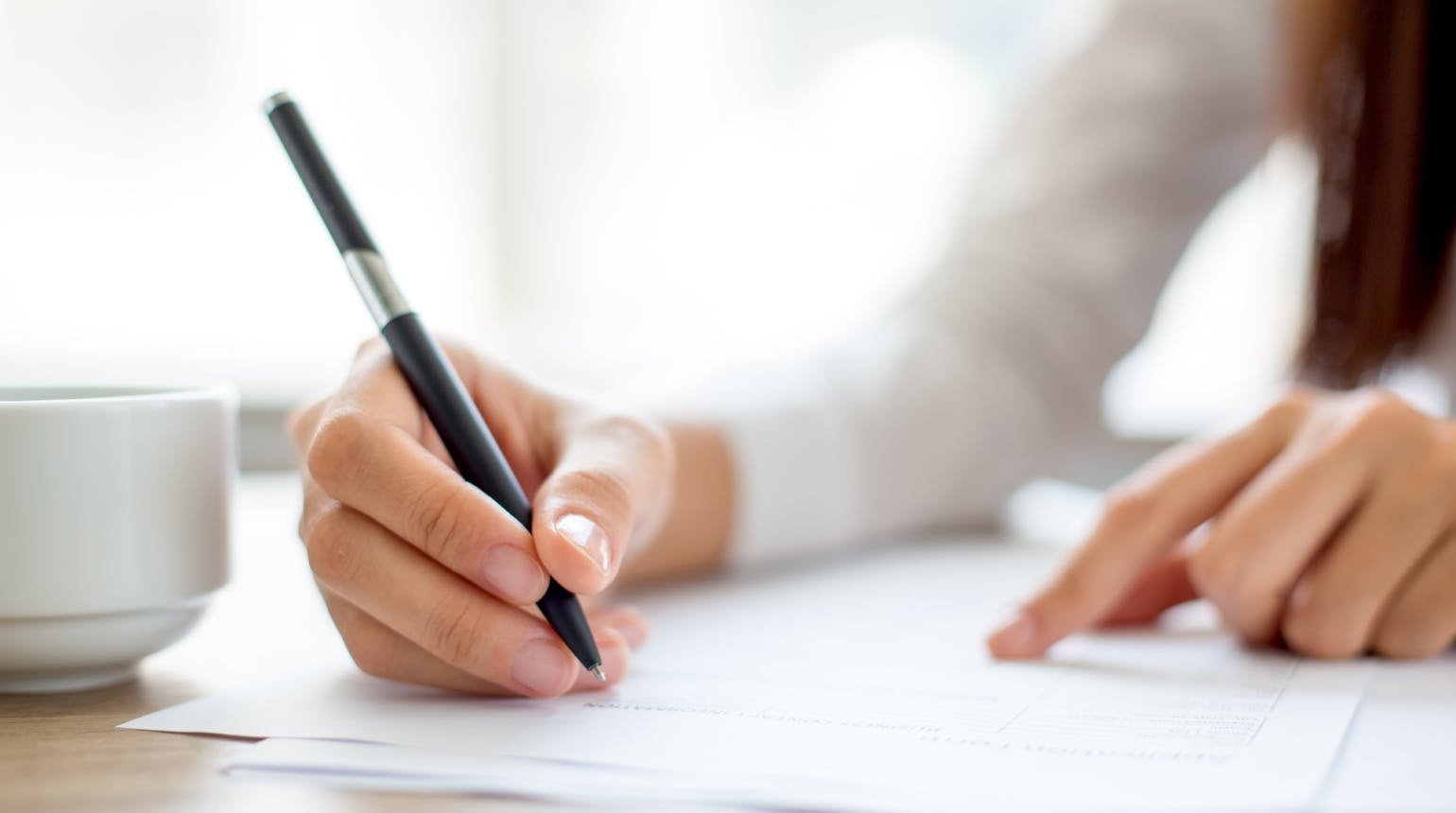 Hand of businesswoman writing on paper in office Hand of businesswoman writing on paper in office