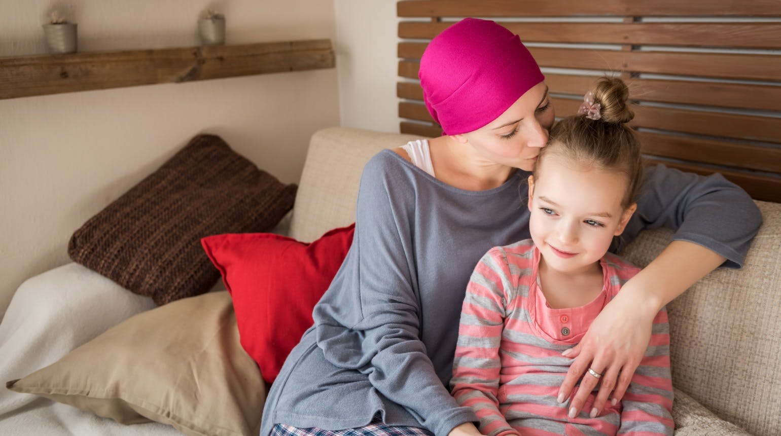 Young adult female cancer patient spending time with her daughter at home, relaxing on the couch