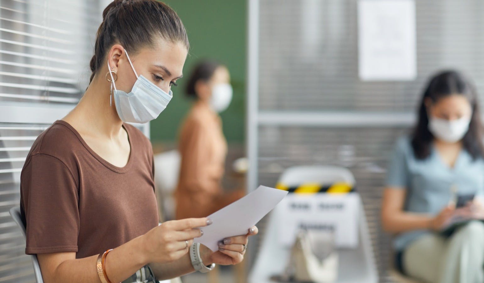 young woman wearing mask and holding document while waiting in line in office young woman wearing mask and holding document while waiting in line in office