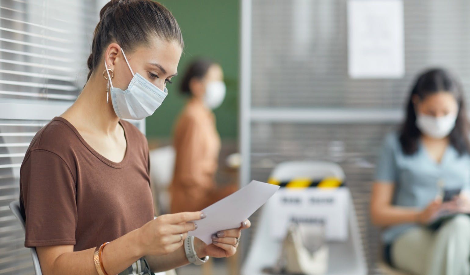 young woman wearing mask and holding document while waiting in line in office