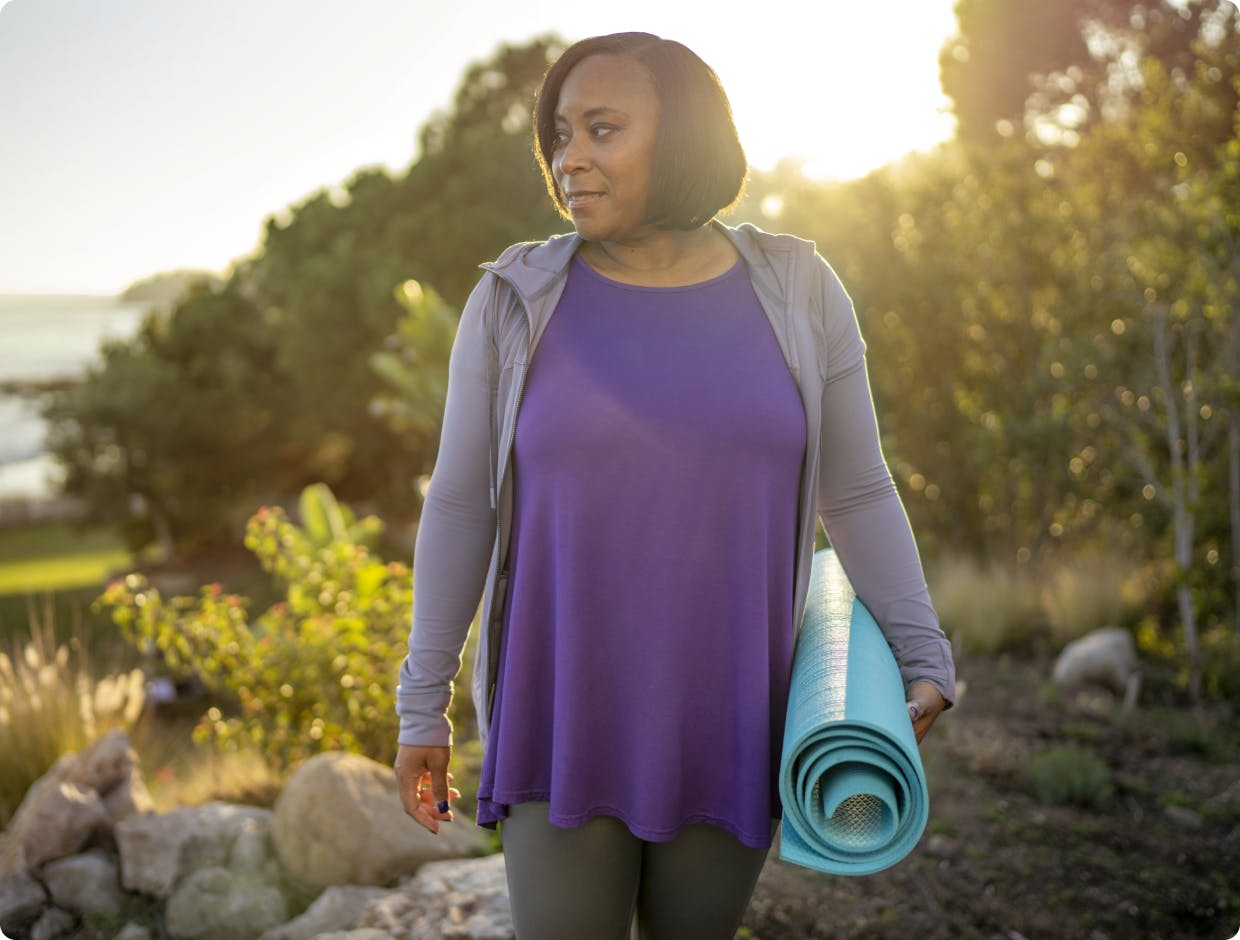 BENLYSTA patient Racquel walking outside holding a yoga mat. 