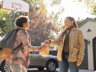 Mother handing a brown bag lunch to her son in their driveway