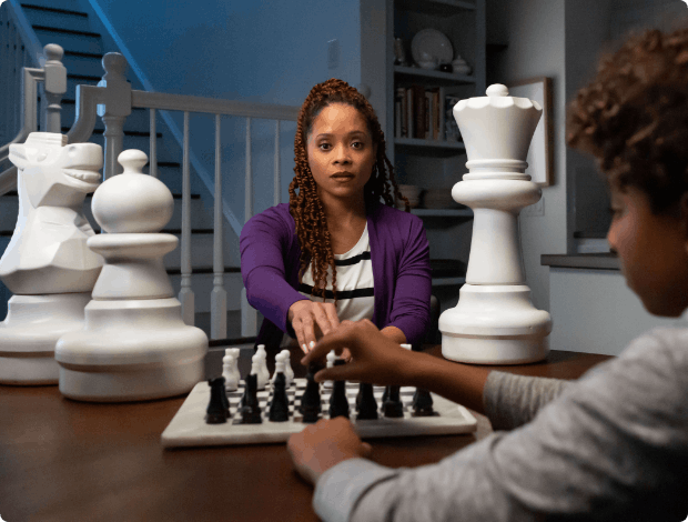 Mother playing chess with her son next to large white chess pieces