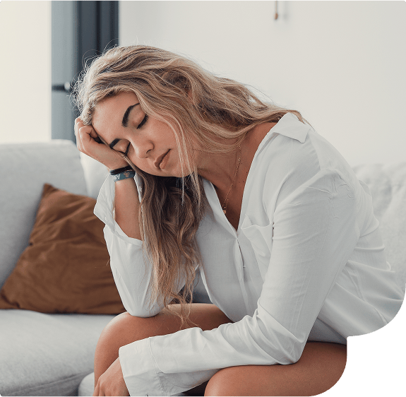 Mulher sentada no sofá apoiando a cabeça na mão com cara de cansada.