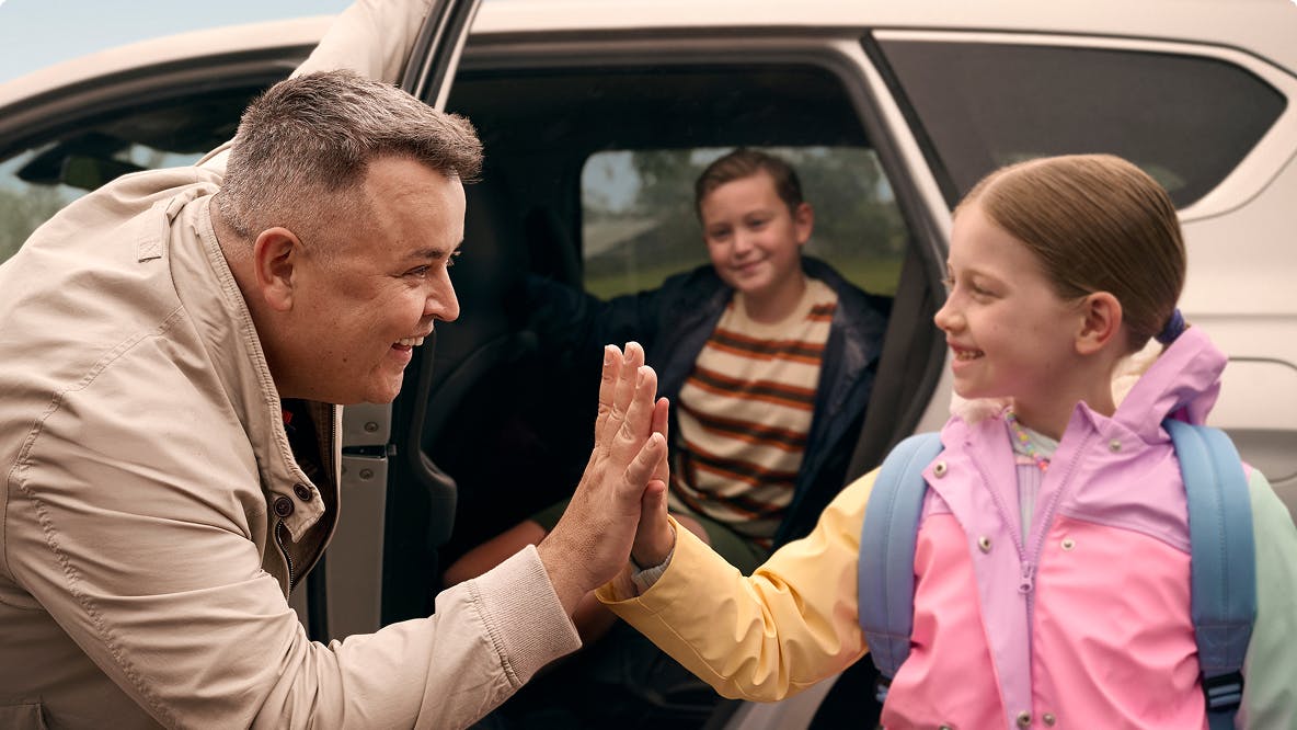 Man high fiving daughter outside of car with son in background