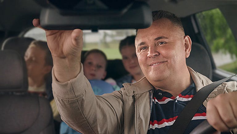 Man looking at three children in the backseat of a car using a rearview mirror