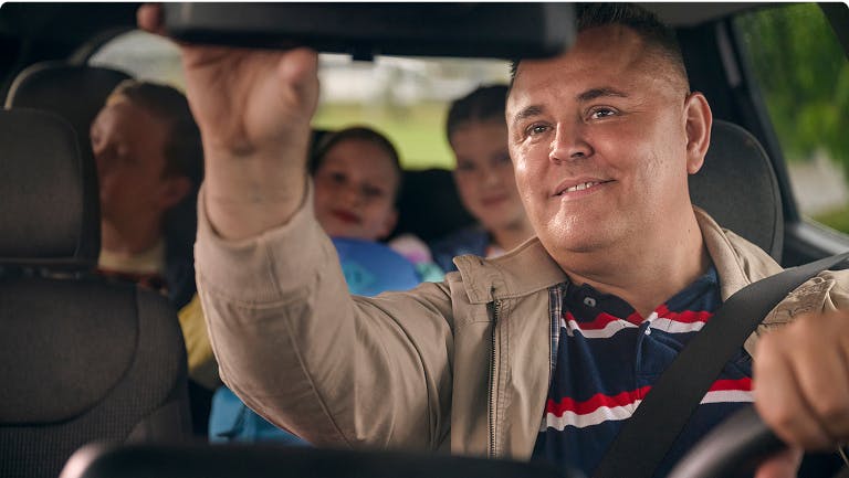 Man looking at three children in the backseat of a car using a rearview mirror