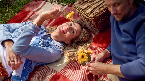 Man and woman lying on picnic blanket holding yellow flowers