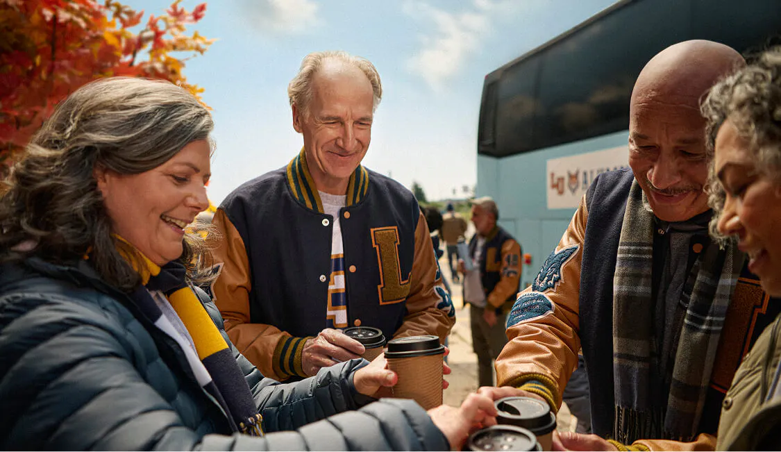 Two older couples holding portable coffee cups while standing outside of a tour bus