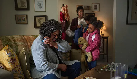 Older woman sitting on a couch coughing while holding a rescue inhaler as her granddaughter looks concerned