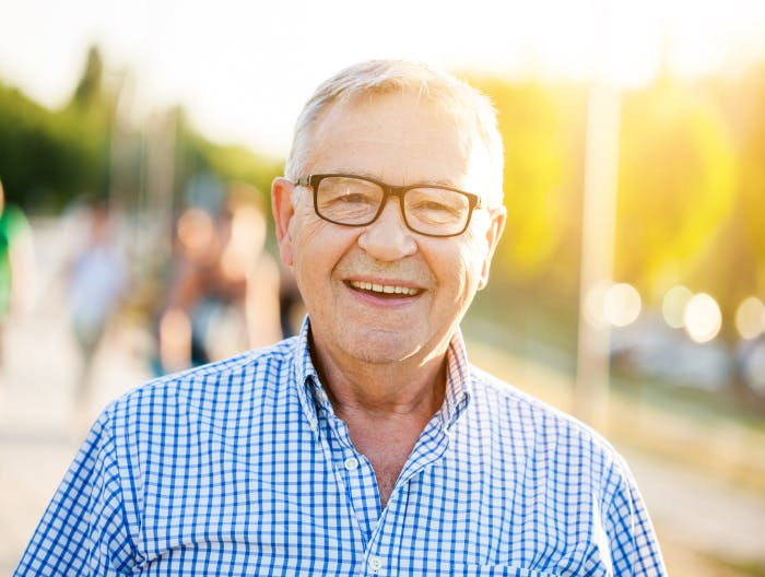 Älterer Herr mit Brille, der glücklich lächelt, da er trotz seiner HIV Infektion ein großteils normales Leben führt.