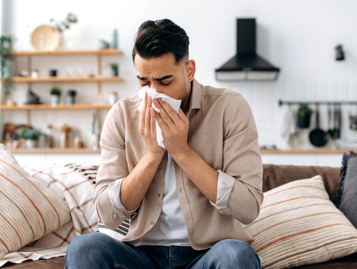 Junger Mann hat Schnupfen und nutzt ein Papiertaschentuch, es ist nicht klar, ob er eine Grippe oder eine HIV-Infektion hat.