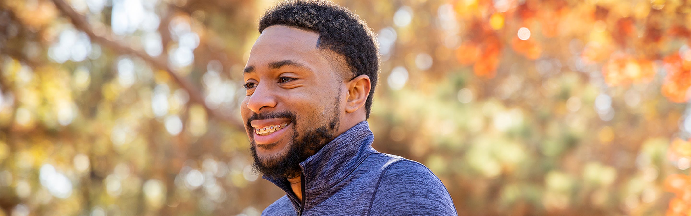 A younger african man with braces smiling while walking in the woods in autumn.