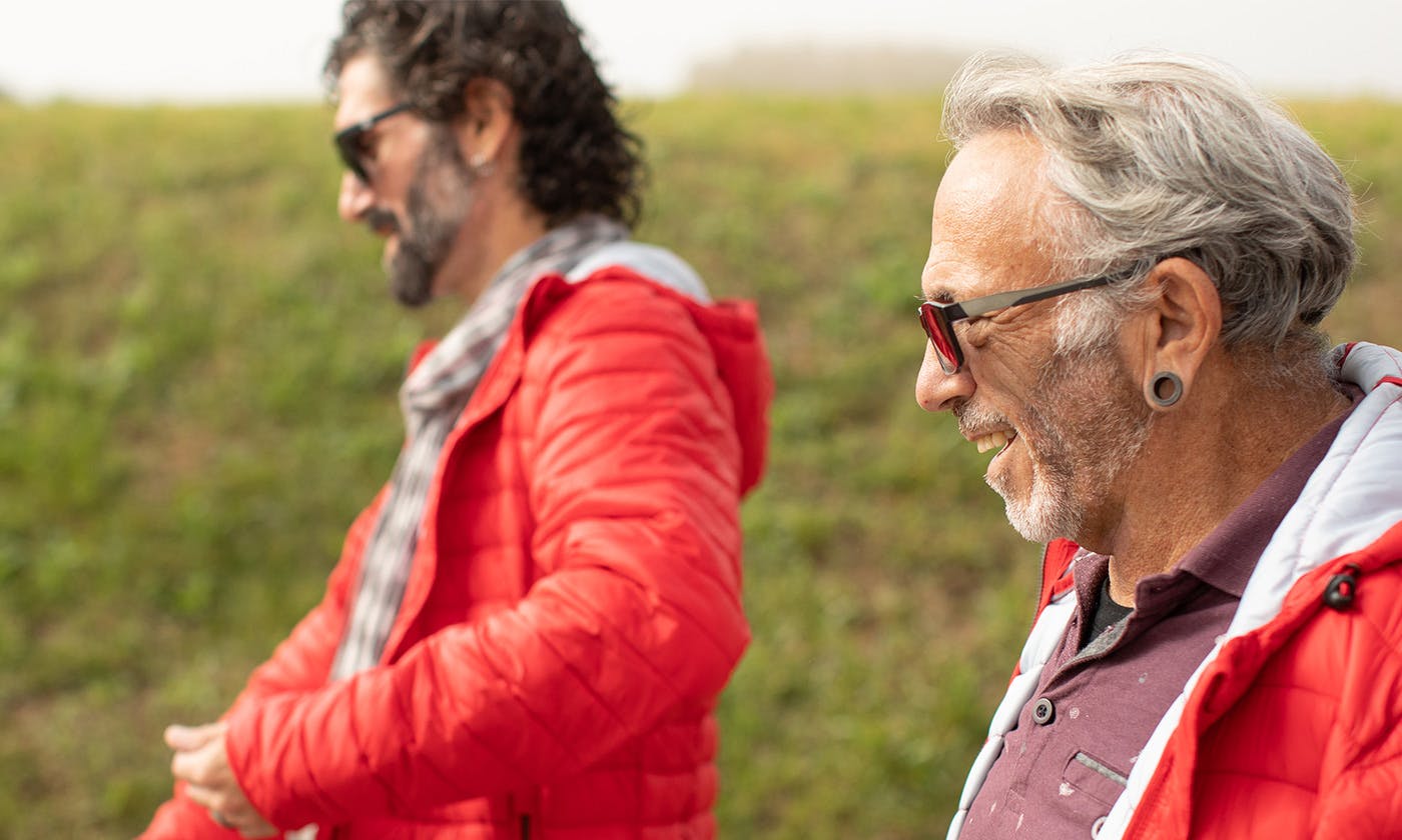 Two causasian men walking outside side profile. Both wearing red puffer jackets and sunglasses.