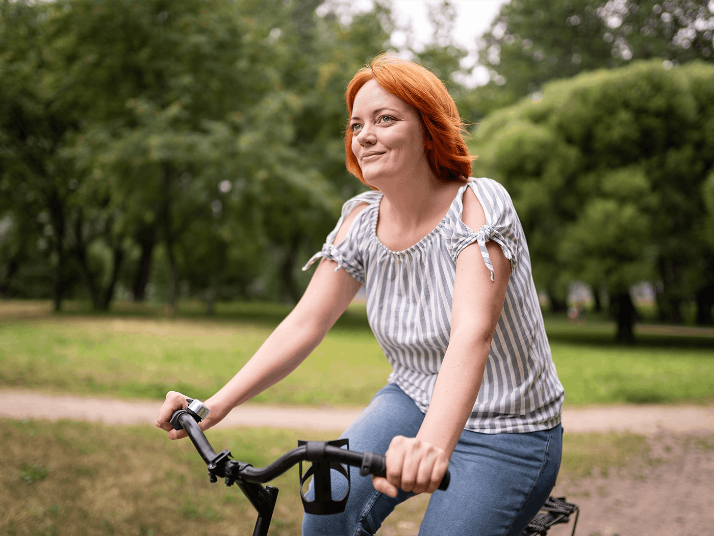 A caucasian woman with orange hair riding a bicycle in the park.