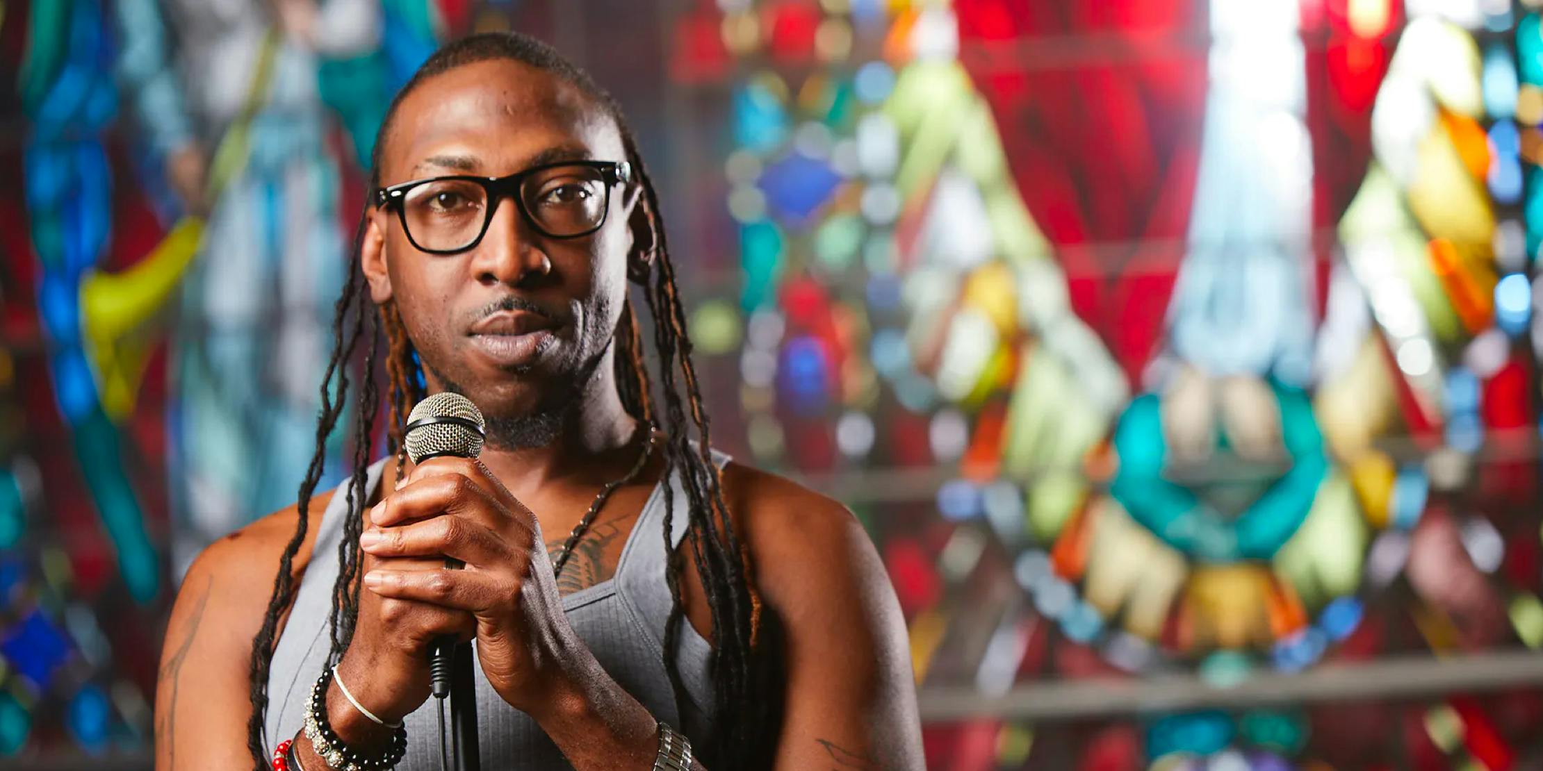 Man stands with a microphone against the backdrop of a stain glassed window in a church