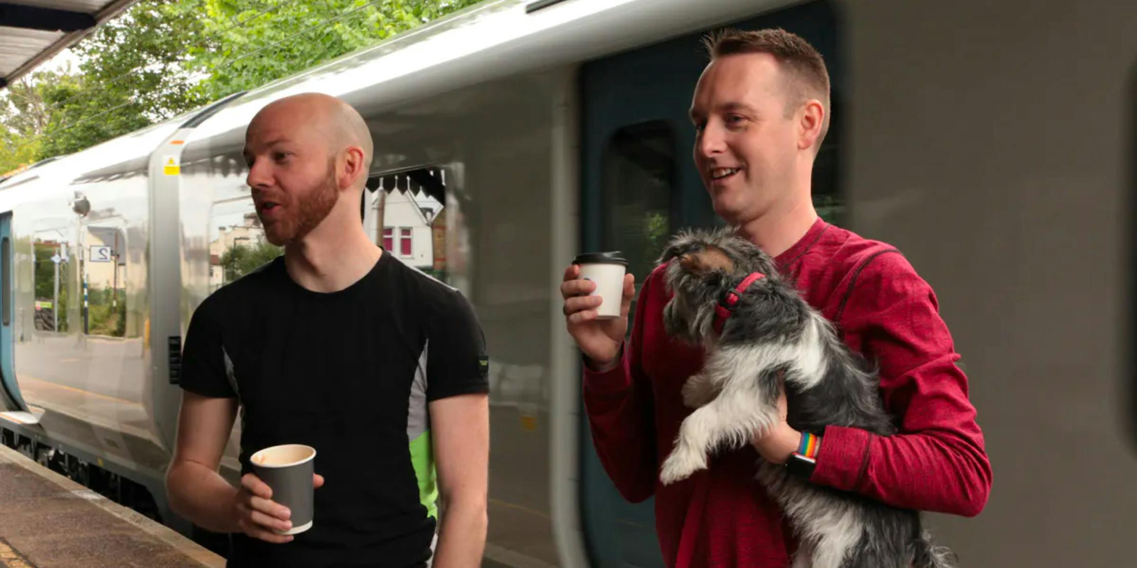 two men standing on train platform, one holding a dog