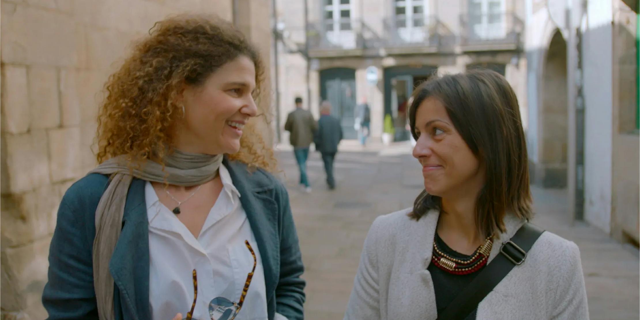 two women smiling at each other walking outside together