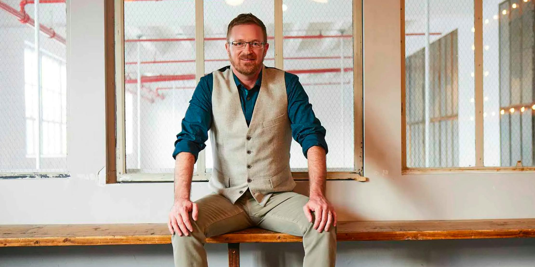 A man sits on a wooden bench and smiles at the camera