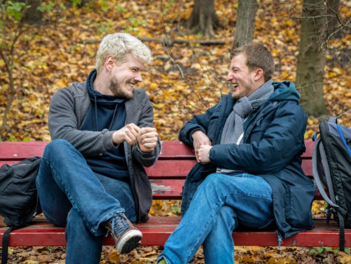 Dos hombres sentados en un banco hablando y sonriendo