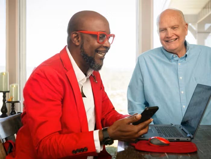 Homme noir vivant avec le VIH travaillant de chez lui sur son ordinateur portable accompagné de son partenaire